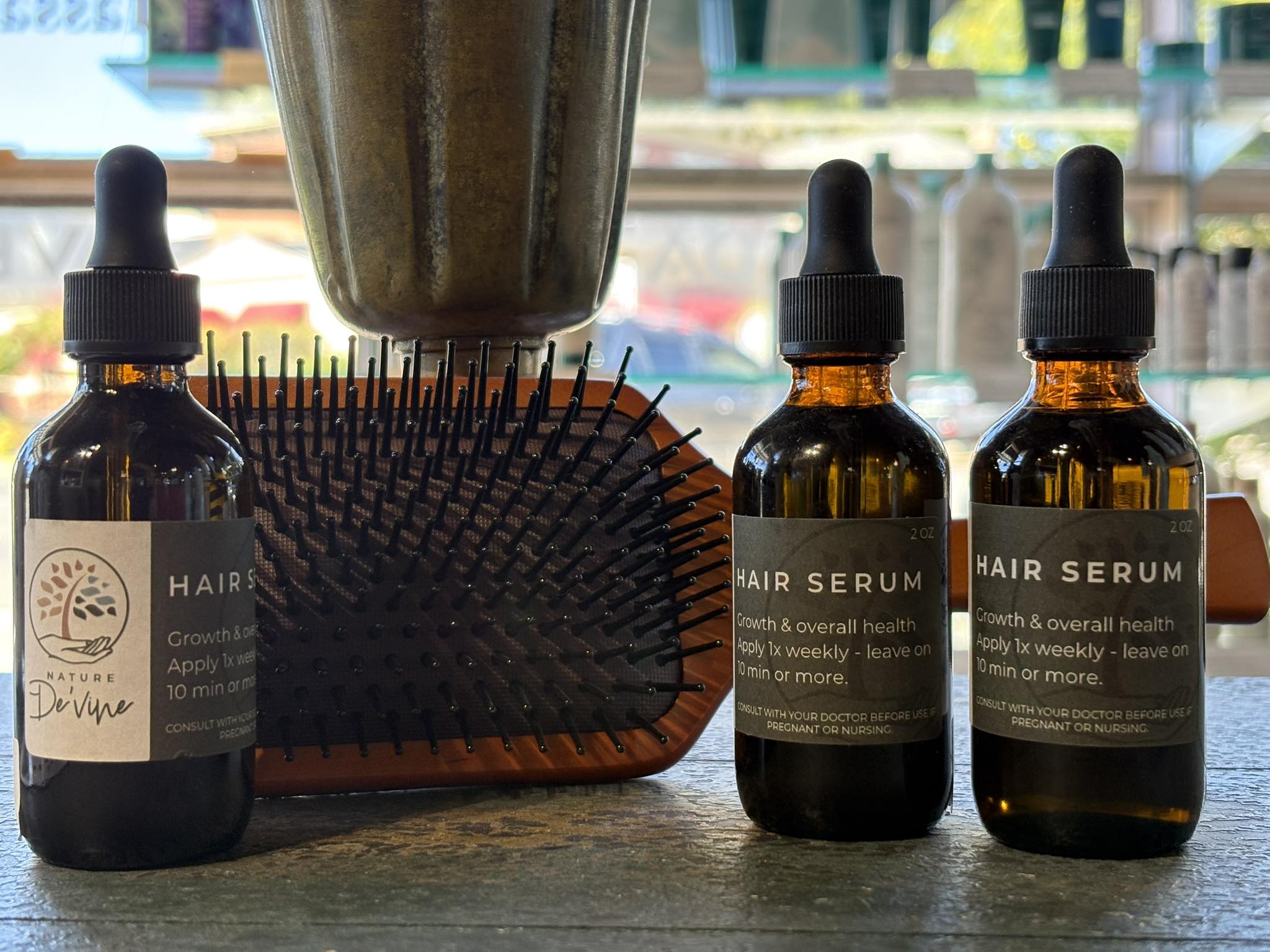 Three bottles of hair serum with a hairbrush on a surface.
