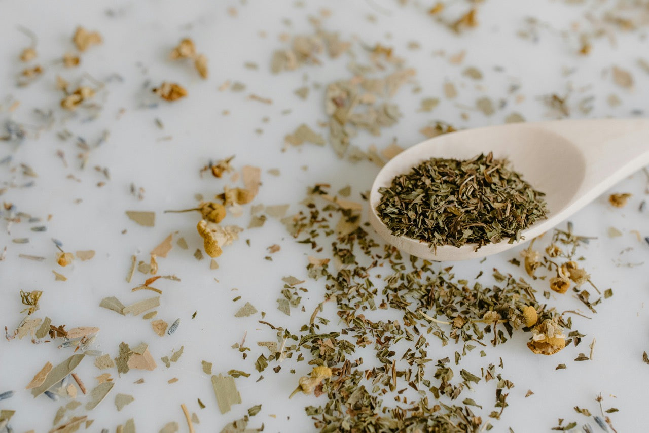 Loose leaf tea on a wooden spoon laying on a surface that has loose leaf tea scattered. 